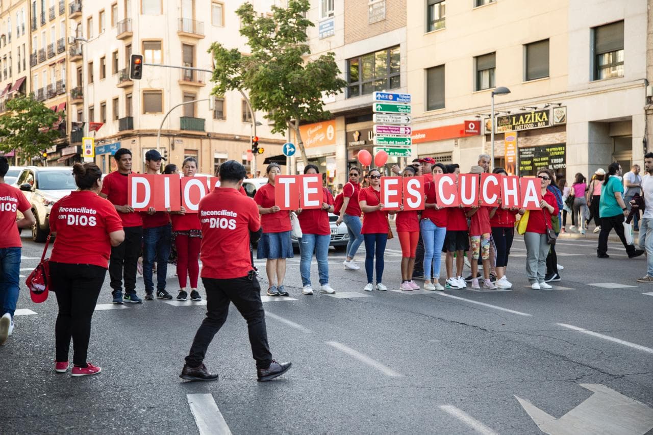 Voluntarios de la iglesia sostienen carteles que forman la frase «Dios te escucha» en una calle